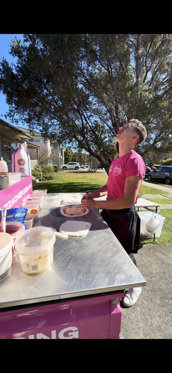 Matteo singing while preparing pizza at his pink outdoor catering station